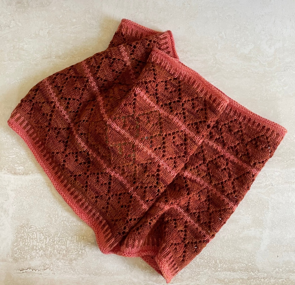 handknit cowl in rust colored tones with a lace pattern of repeated diamonds on a marble background