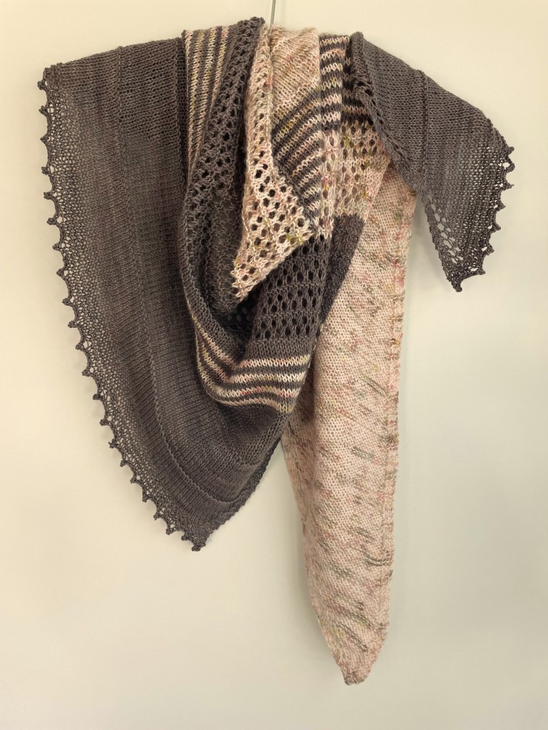 two-toned taupe and speckled pink and green hand knit shawl on on wooden hanger